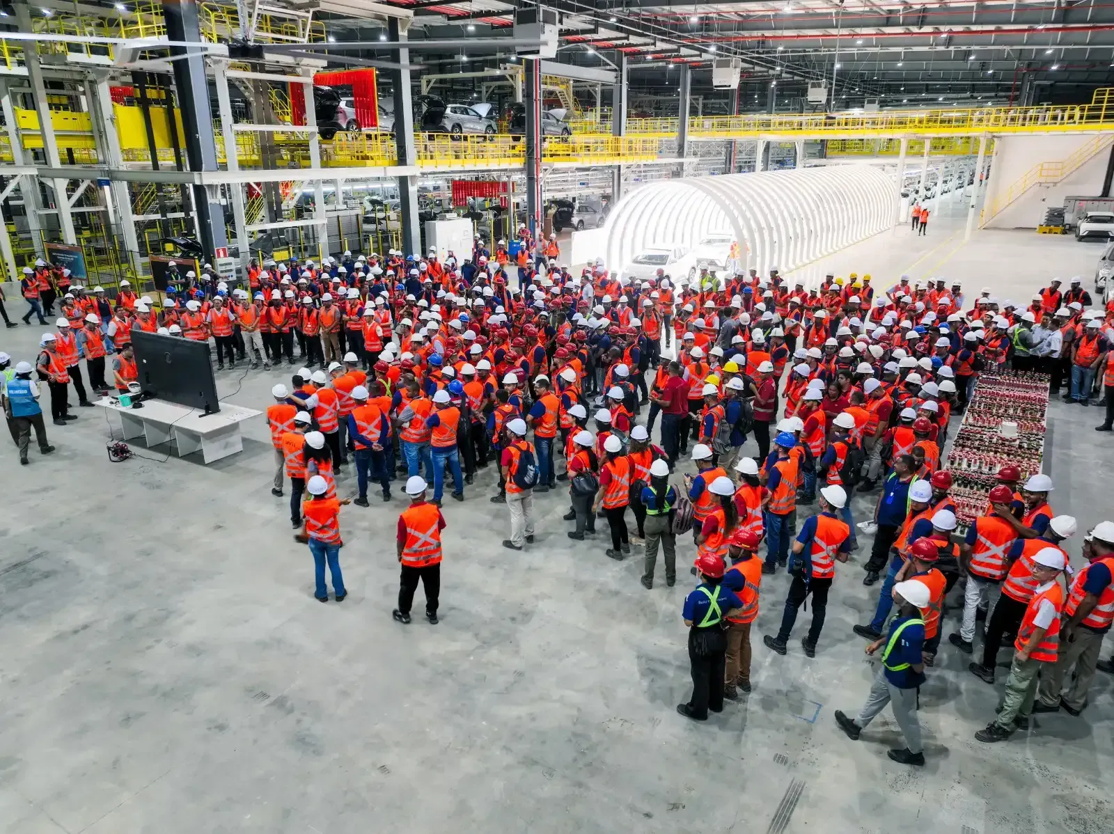 Centenas de funcionários de uniforme laranja reunidos dentro da fábrica da BYD em Camaçari