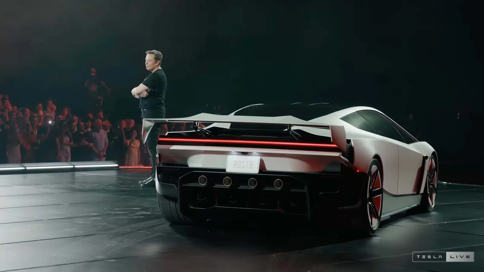 Traseira do Tesla Roadster com asa traseira, ao lado de Elon Musk